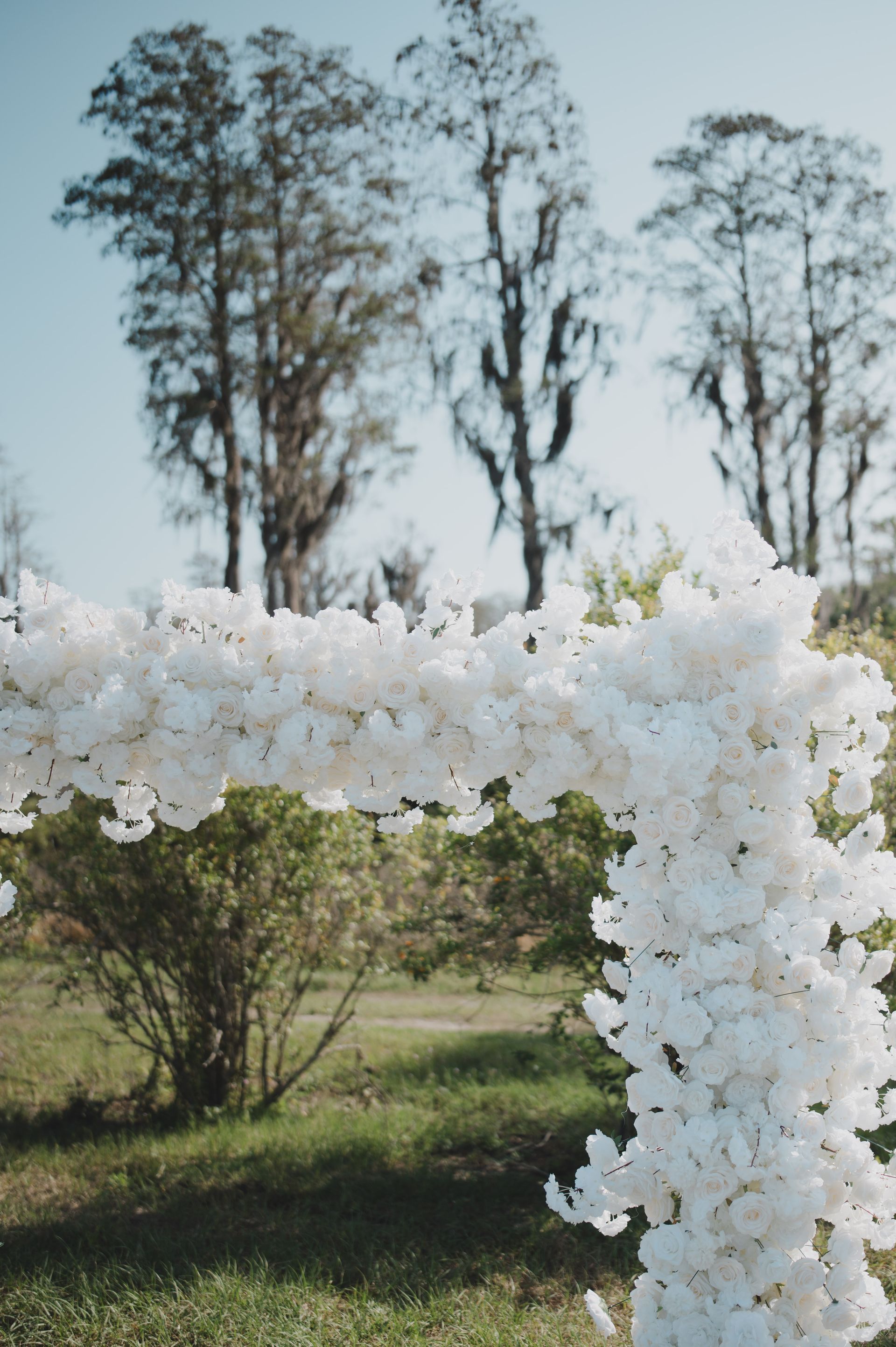 A white arch made of white flowers is sitting in the grass.