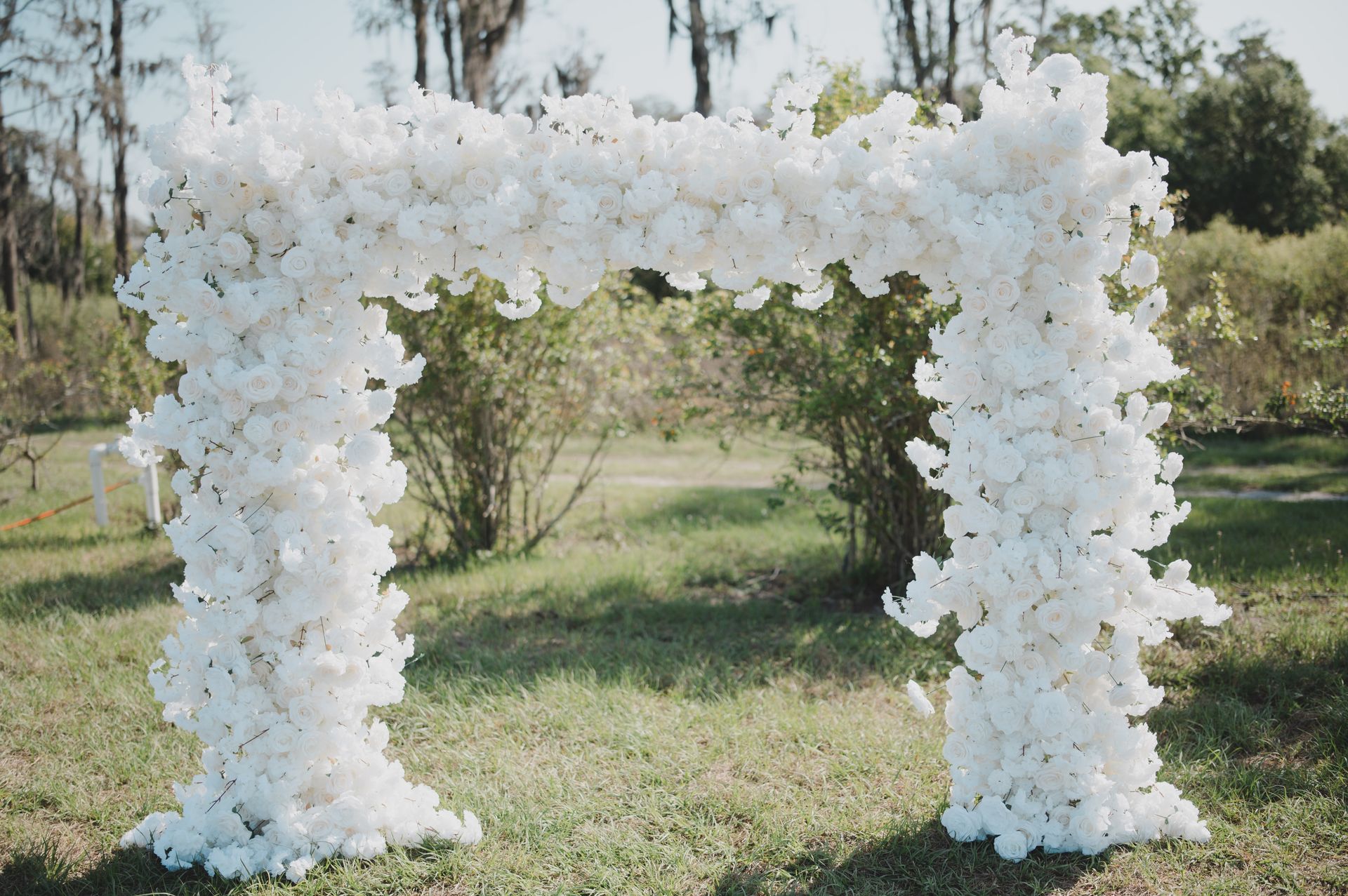 A white arch made of white flowers is sitting in the grass.