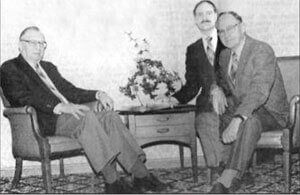 A black and white photo of three men sitting around a table.