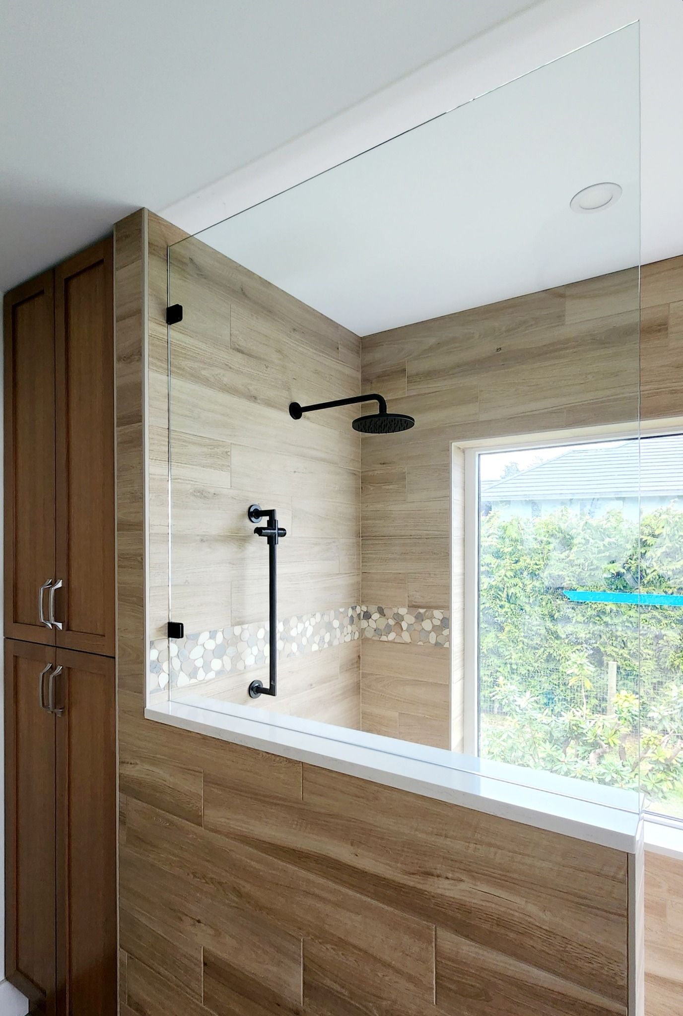A bathroom with a walk in shower with a glass door and a window.