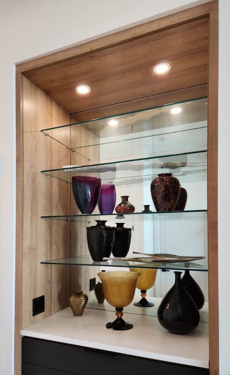 A glass shelf filled with vases and bowls in a room.
