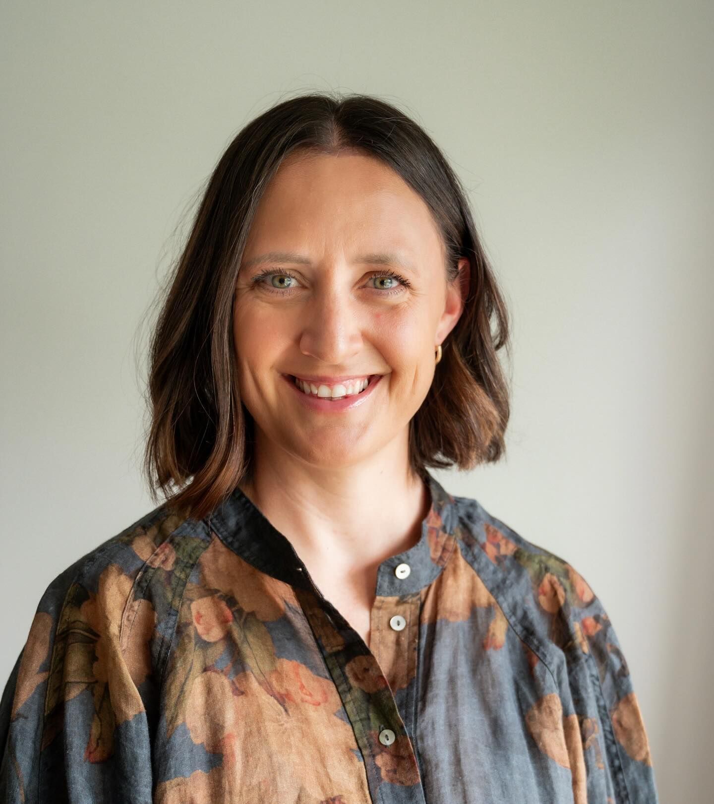 A smiling person with
brown hair, wearing a loose-fitting floral top against a plain light  Professional Travel agent 
