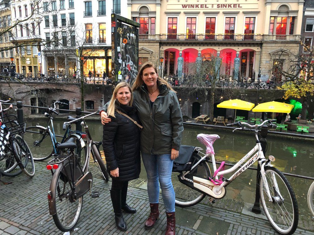 Two women are standing next to each other next to bicycles.