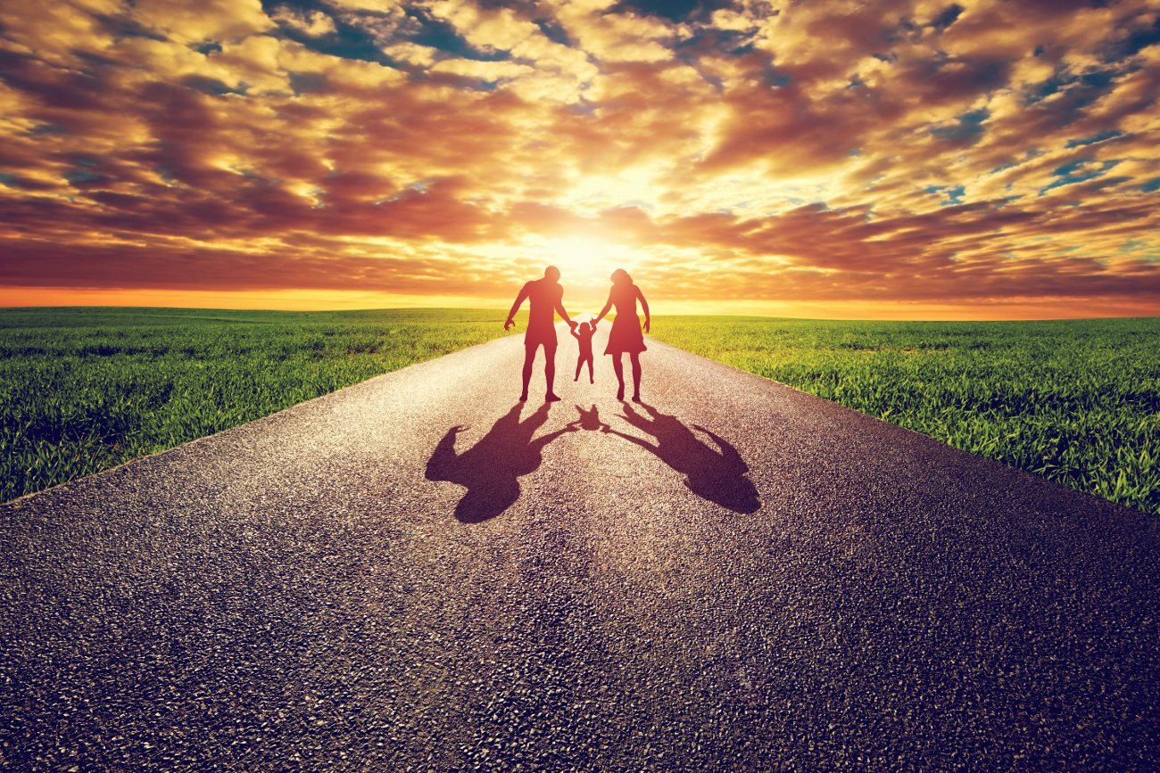 A family is walking down a road holding hands at sunset.