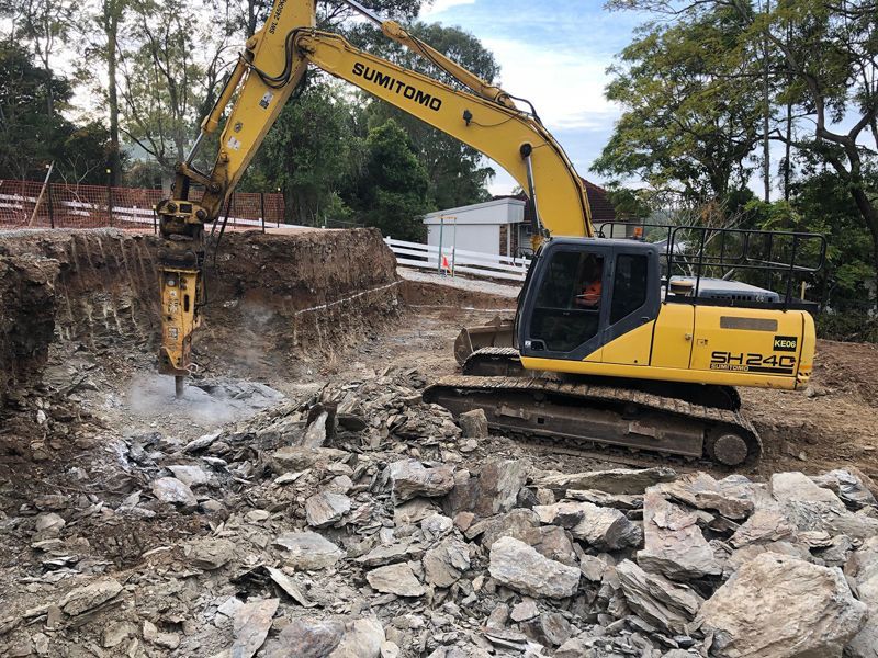 A yellow excavator is breaking rocks on a construction site.