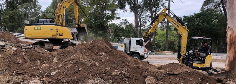 Two excavators are working on a pile of dirt next to a truck.