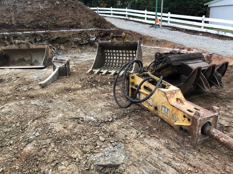 A yellow hydraulic hammer is sitting on top of a dirt field.