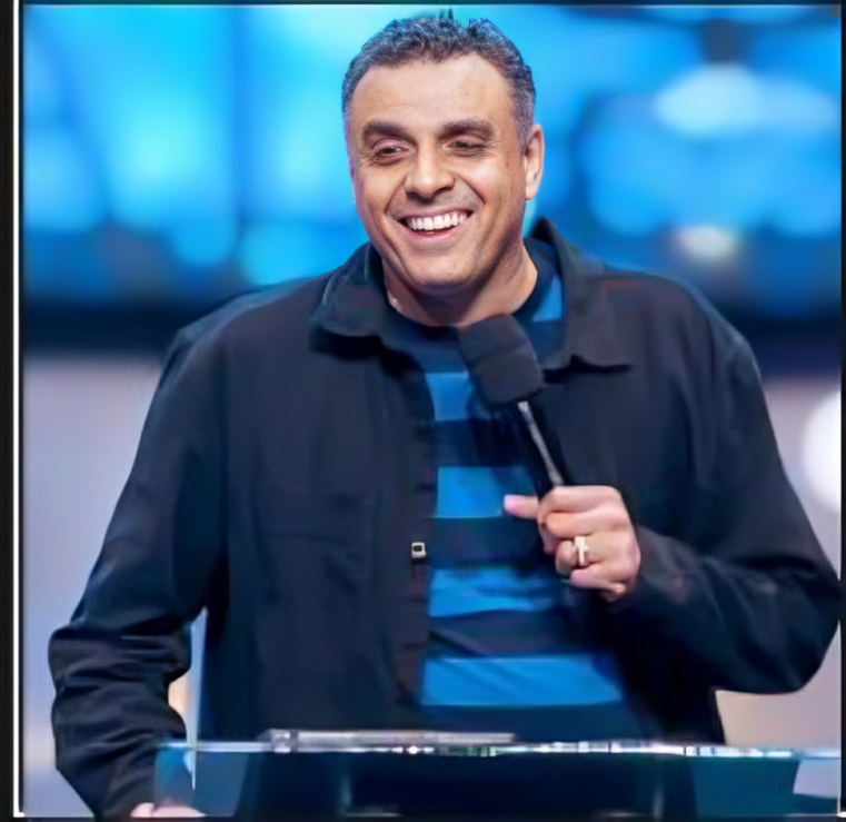 A man is standing at a podium holding a microphone and smiling.