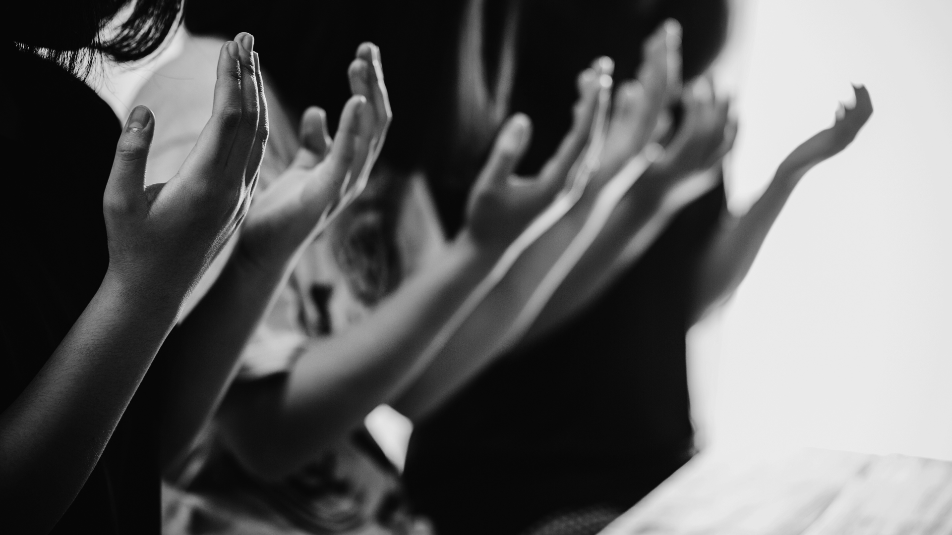 A group of people are raising their hands in the air in a black and white photo.