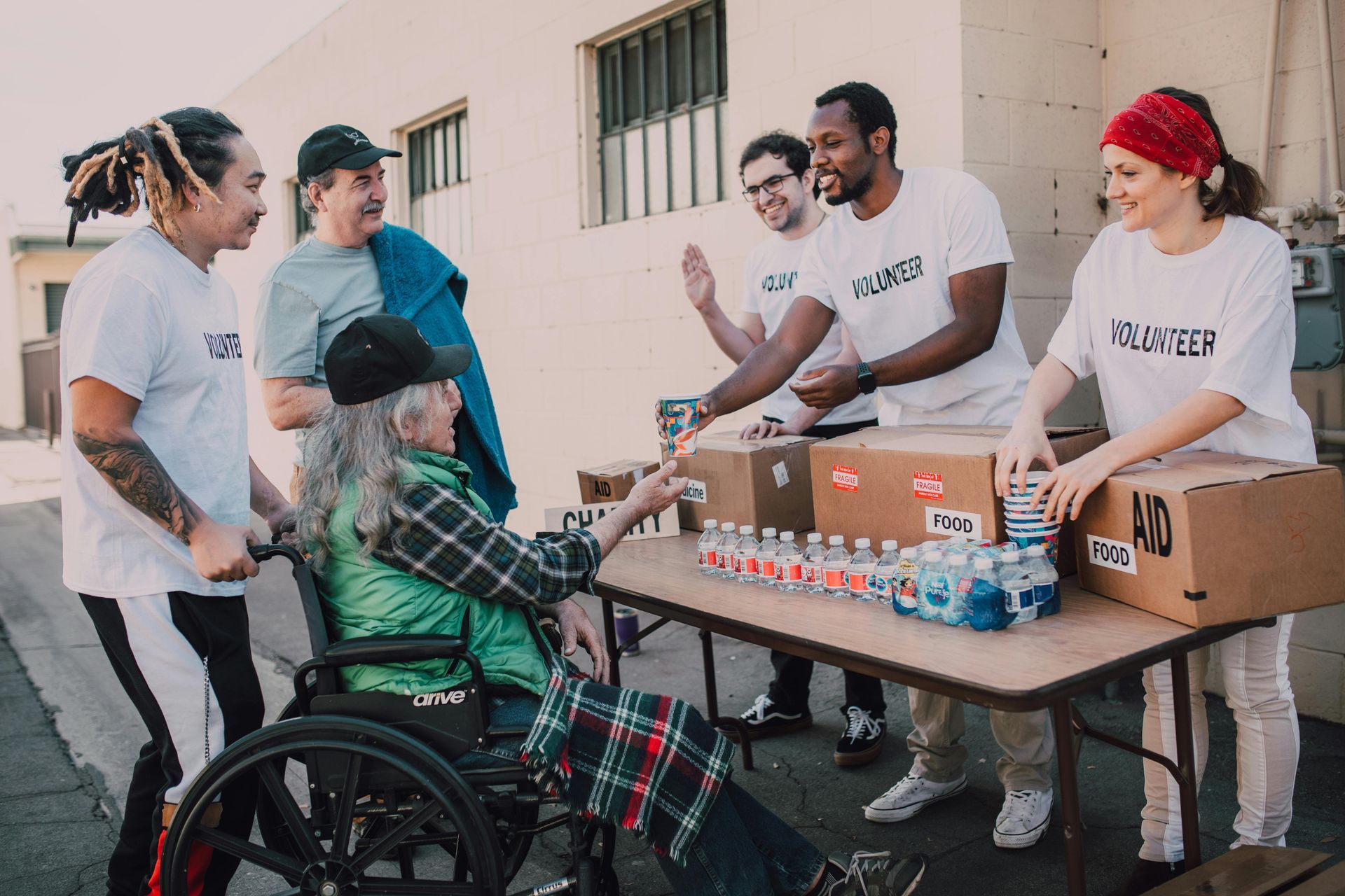 A group of volunteers are helping an elderly woman in a wheelchair.