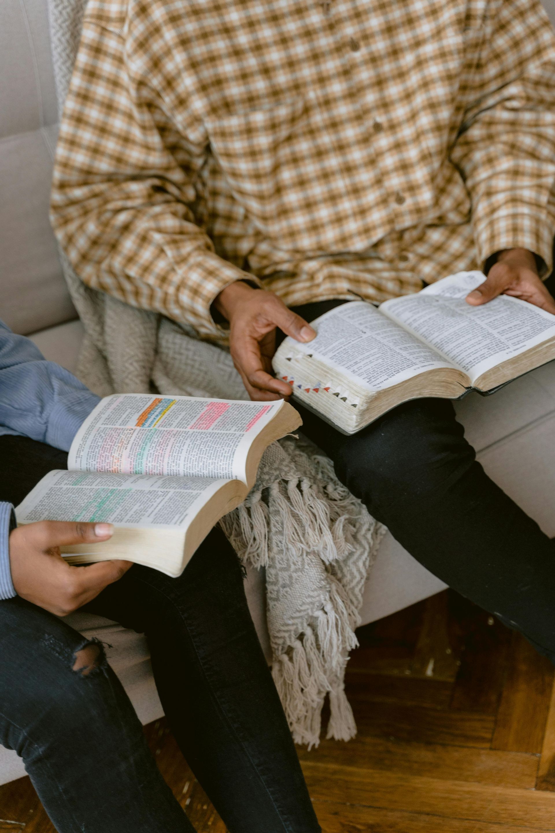 Two people are sitting on a couch reading books.