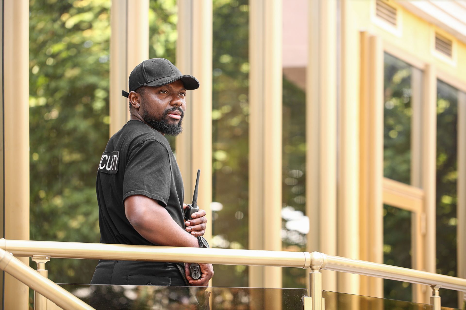 A security guard wearing a black uniform and cap, holding a walkie-talkie.