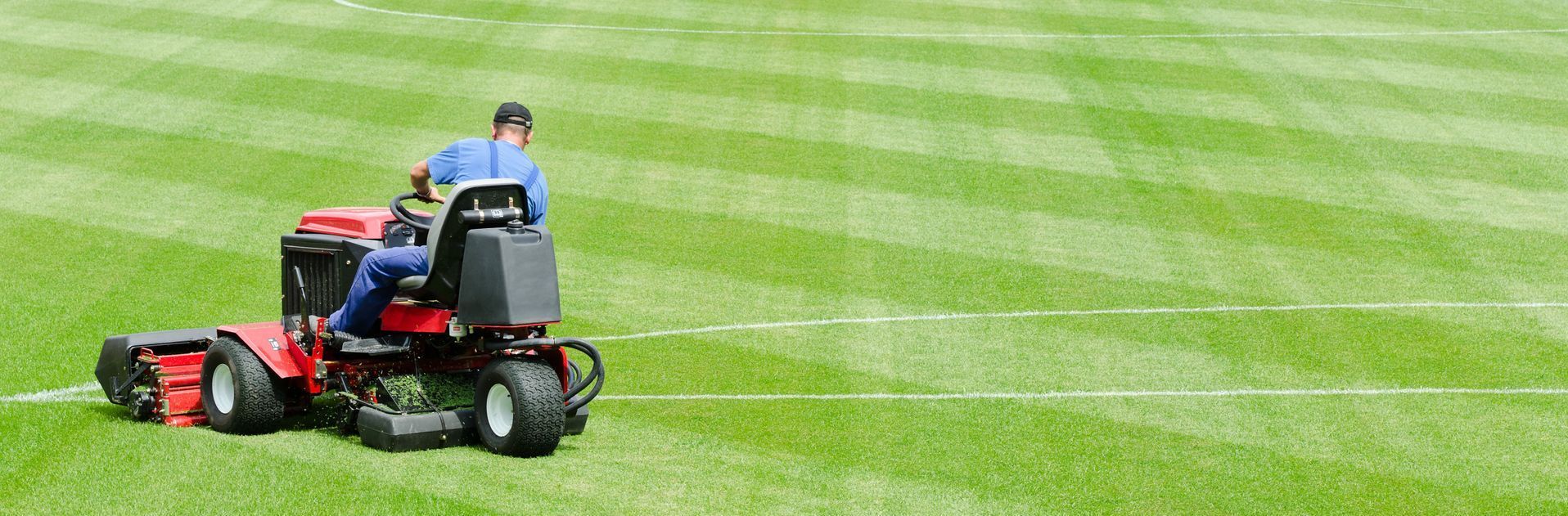 Man on a riding mower cuts grass on a sports field.