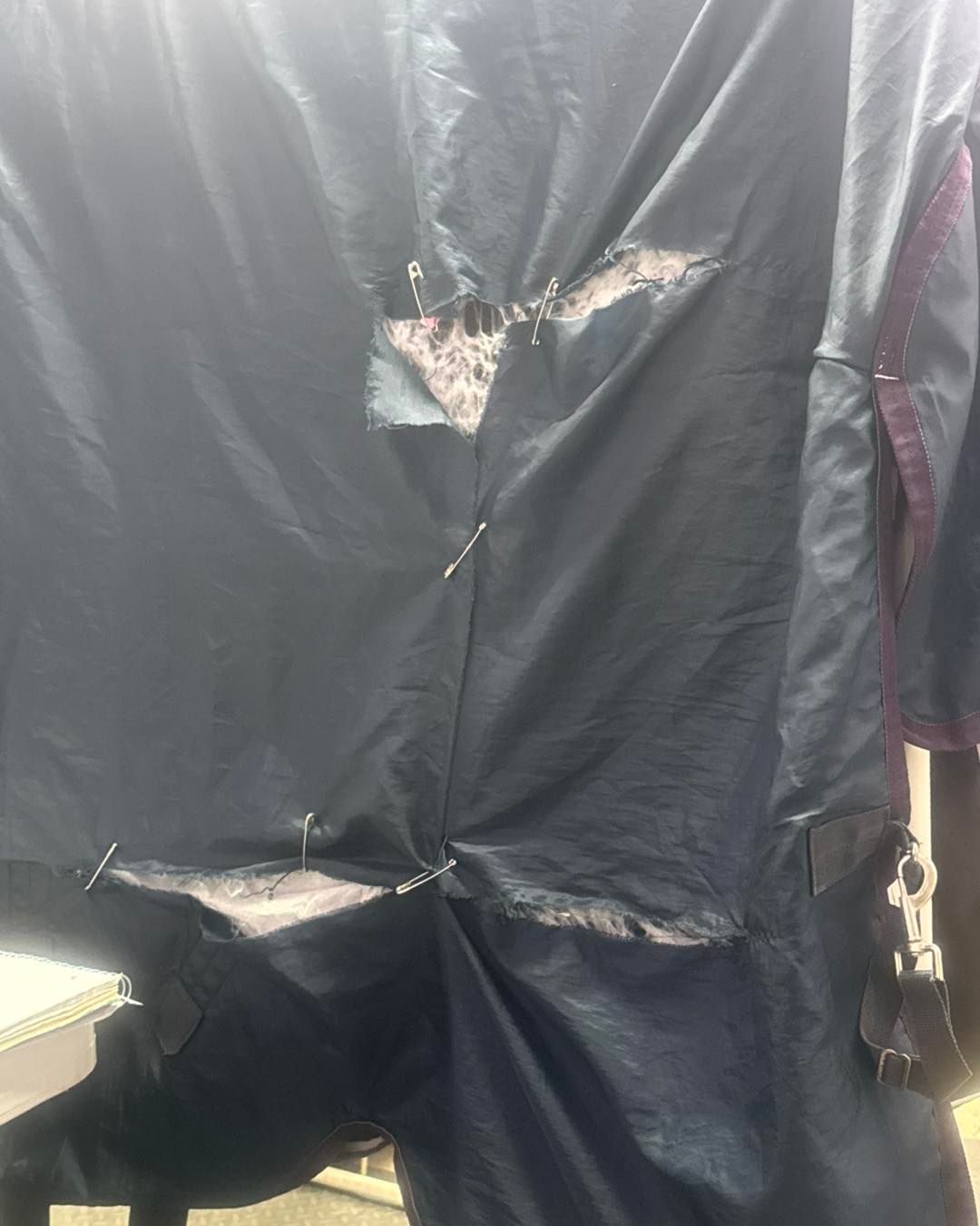 Dark blue tarp with patches and pins, likely for repair, hangs outdoors.