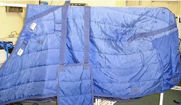 Blue quilted horse blanket with straps, hanging.