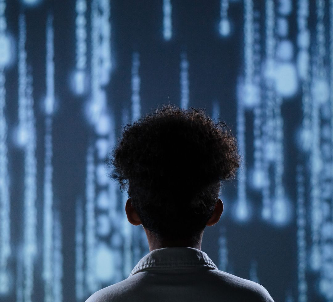 Person gazing at a wall of blurred digital data streams, lit in shades of blue.