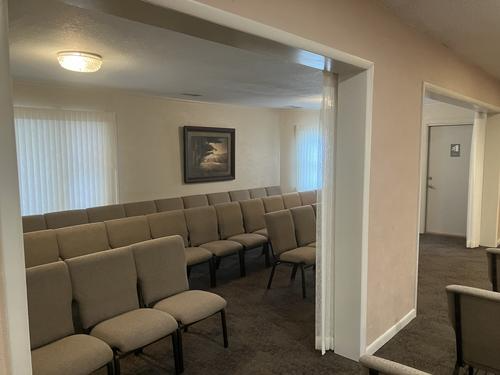 Interior view of a chapel with rows of chairs, windows, and a doorway leading to another room.
