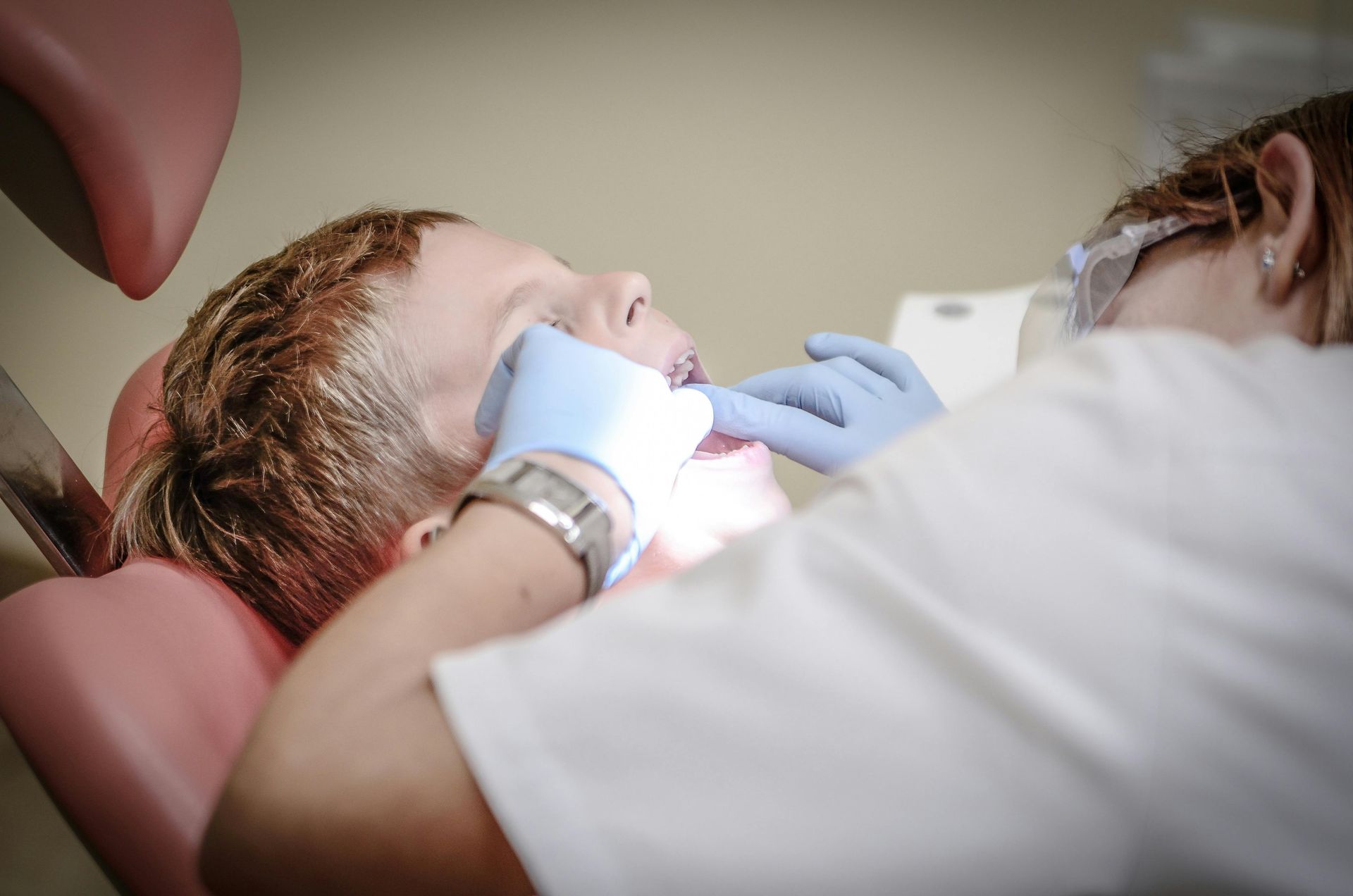 Person in dentist chair with mouth open, receiving dental work. Dentist wears gloves.