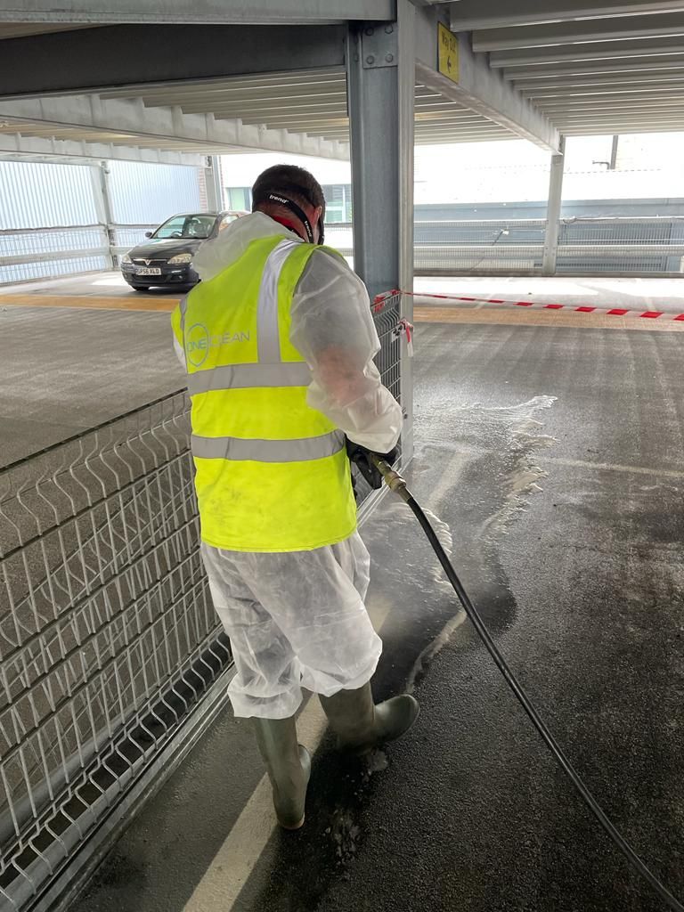 A man in a yellow vest is cleaning a parking garage with a high pressure washer.