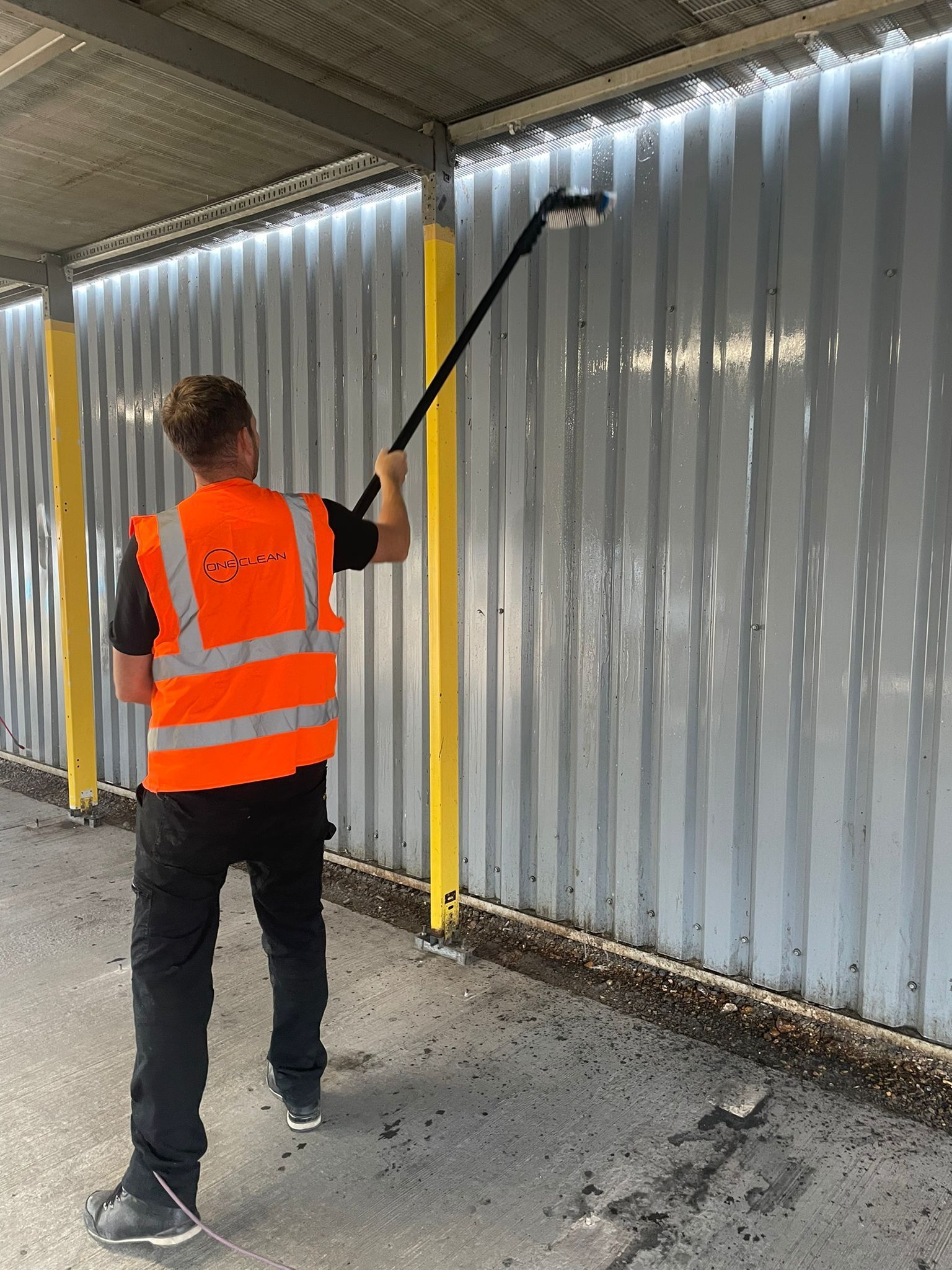 A man in an orange vest is cleaning a wall with a broom.