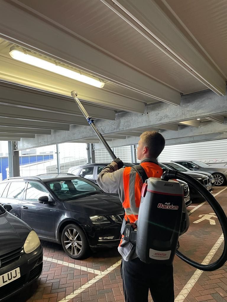 A man is using a vacuum cleaner to clean the ceiling of a parking garage.