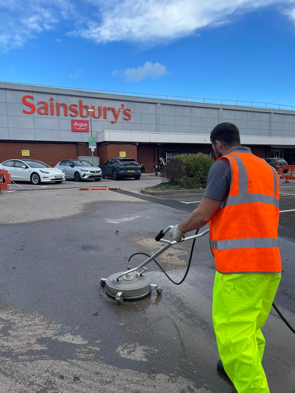 A man is cleaning a parking lot in front of a sainsbury 's store.