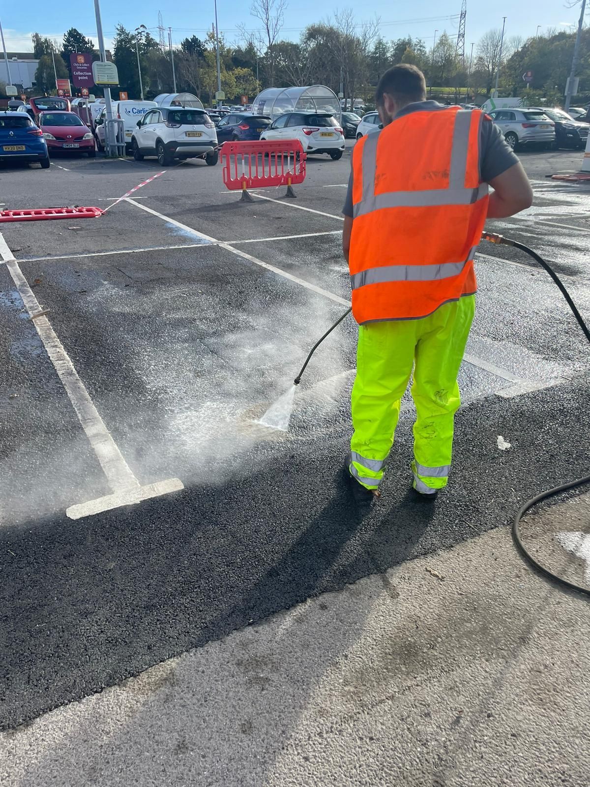 A man is cleaning a parking lot with a high pressure washer.