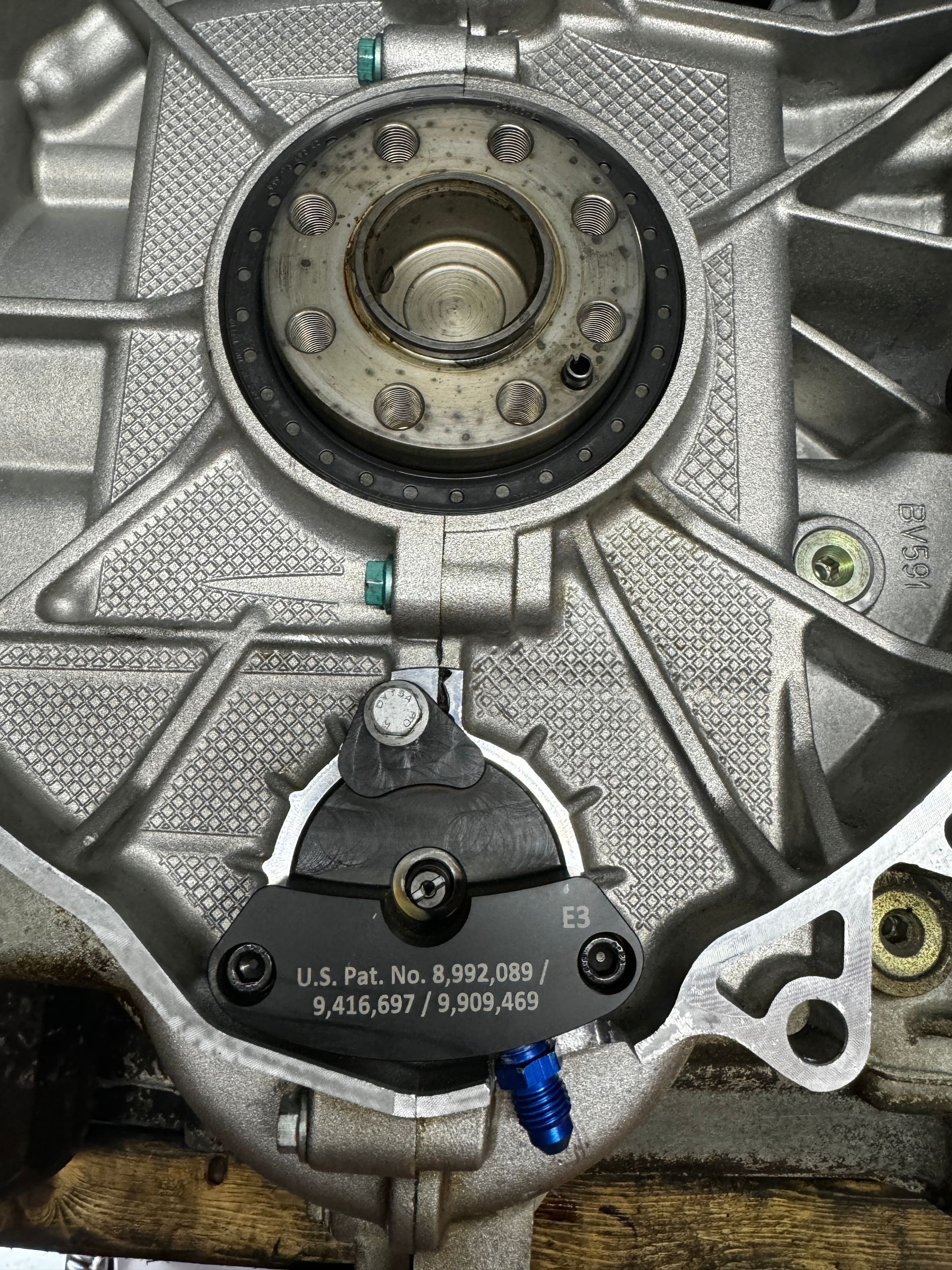 Engine component with a black plate, bolts, and circular seal within a silver casing. | Velocity Motorwerks