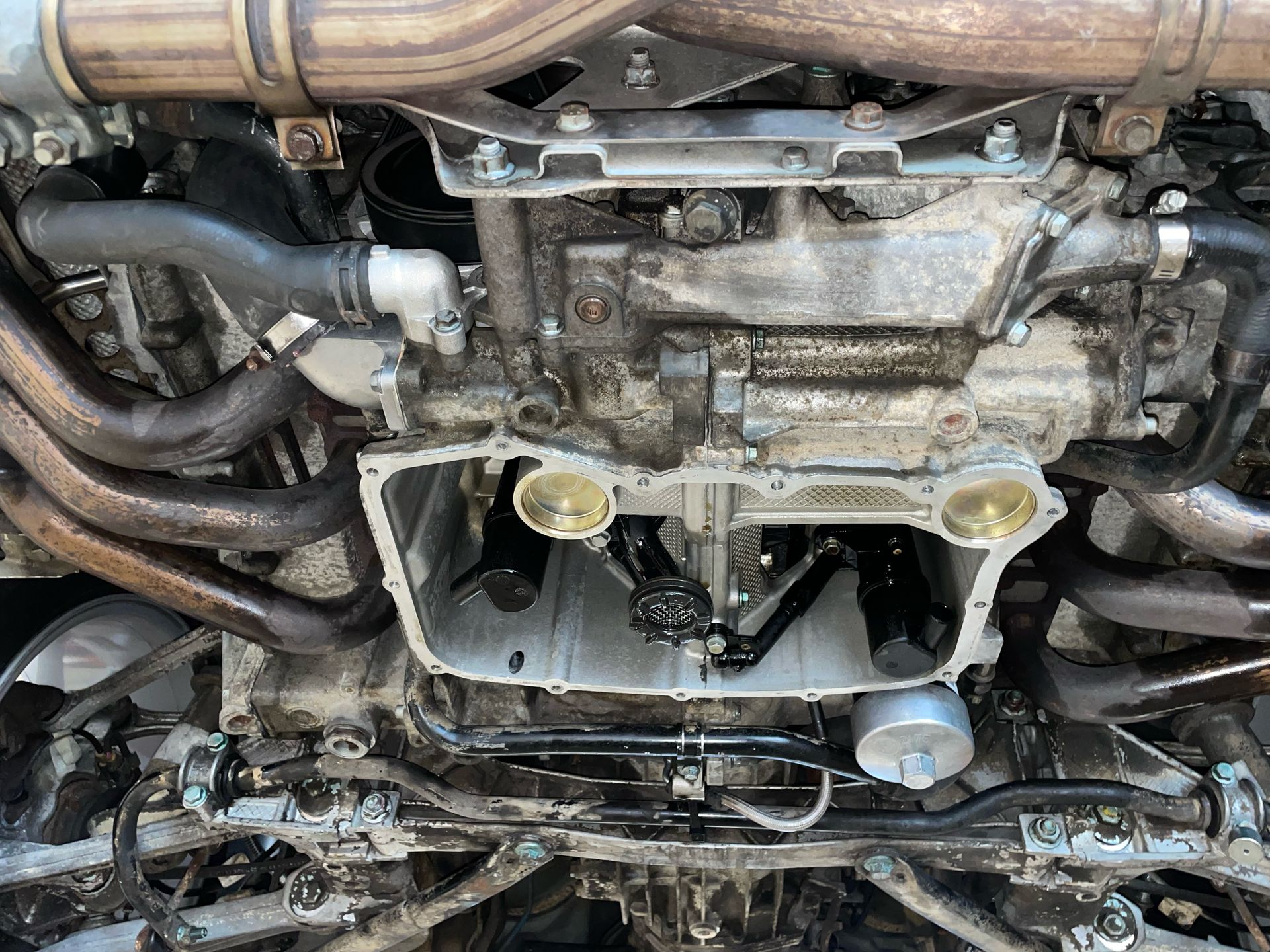 Undercarriage of a vehicle: engine, exhaust pipes, oil filter, and various components with some oily residue. | Velocity Motorwerks