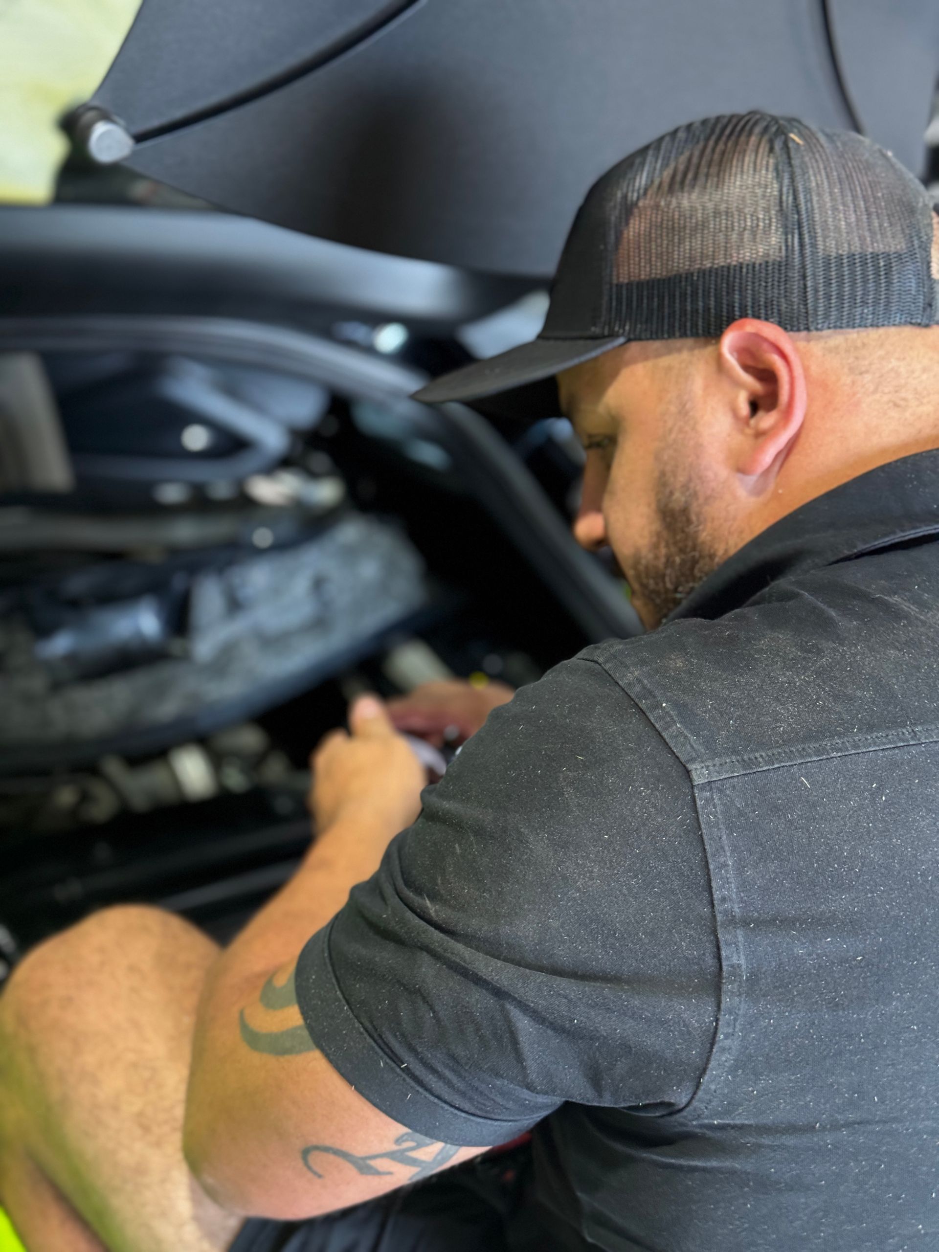 Mechanic working on a car engine, wearing a black cap and shirt. | Velocity Motorwerks