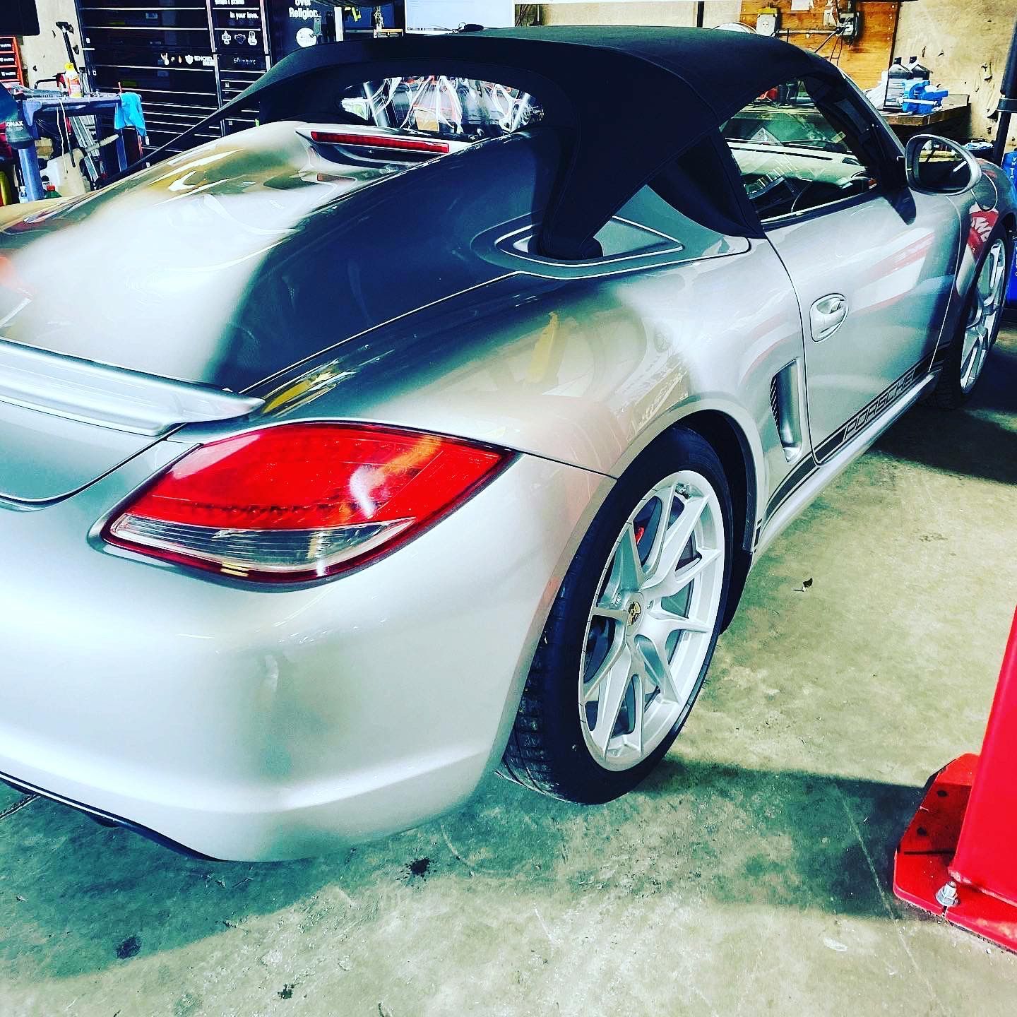 Silver convertible car parked inside a garage with red taillight and black soft top. | Velocity Motorwerks