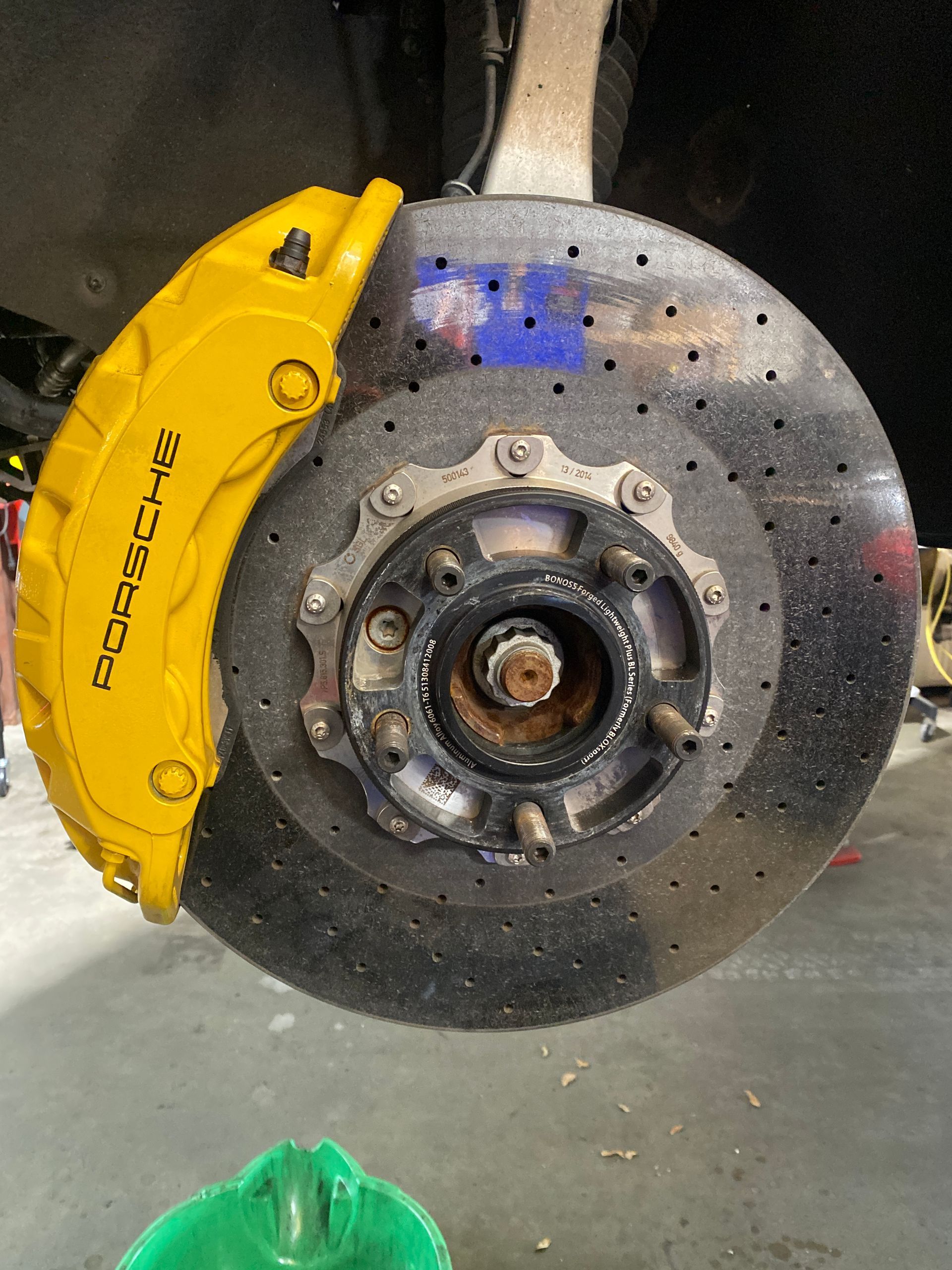 Yellow Porsche brake caliper and rotor on a vehicle, in a garage setting. | Velocity Motorwerks