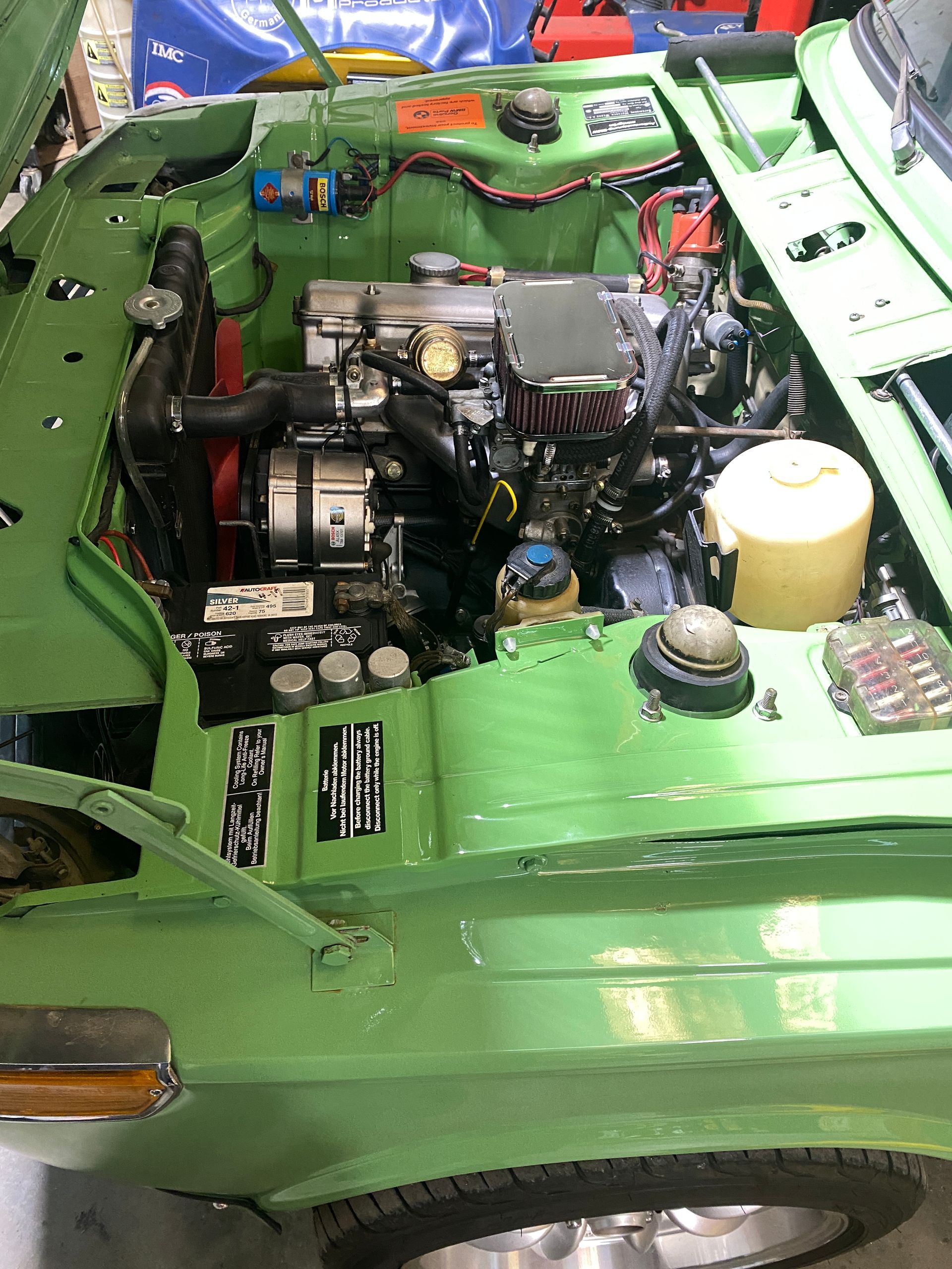 Green car engine bay with a black engine, various wires, and a yellow fluid container. | Velocity Motorwerks