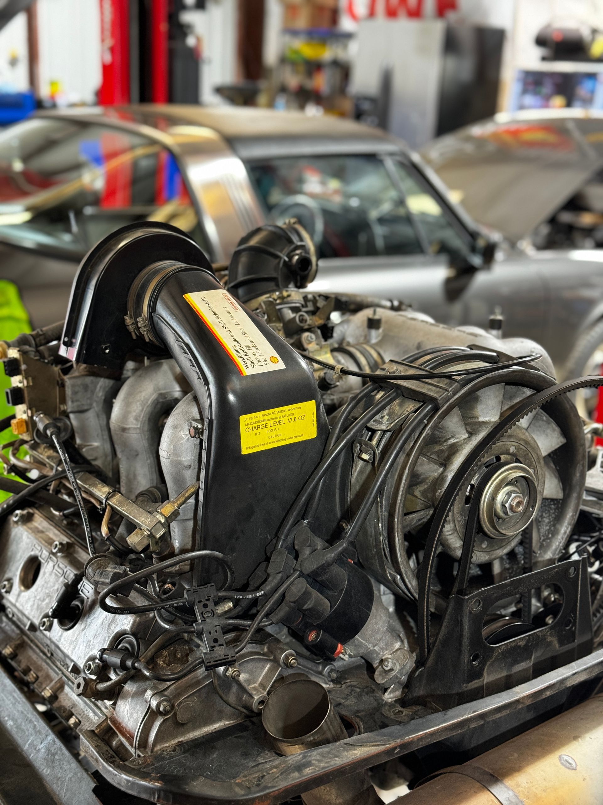 Porsche engine in a garage, black and silver, under a gray car. | Velocity Motorwerks