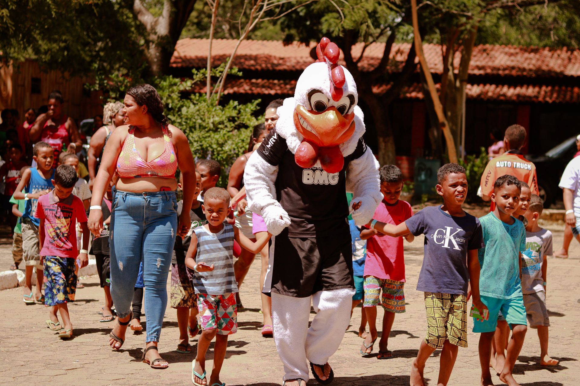 Um mascote de galinha está caminhando com um grupo de crianças.