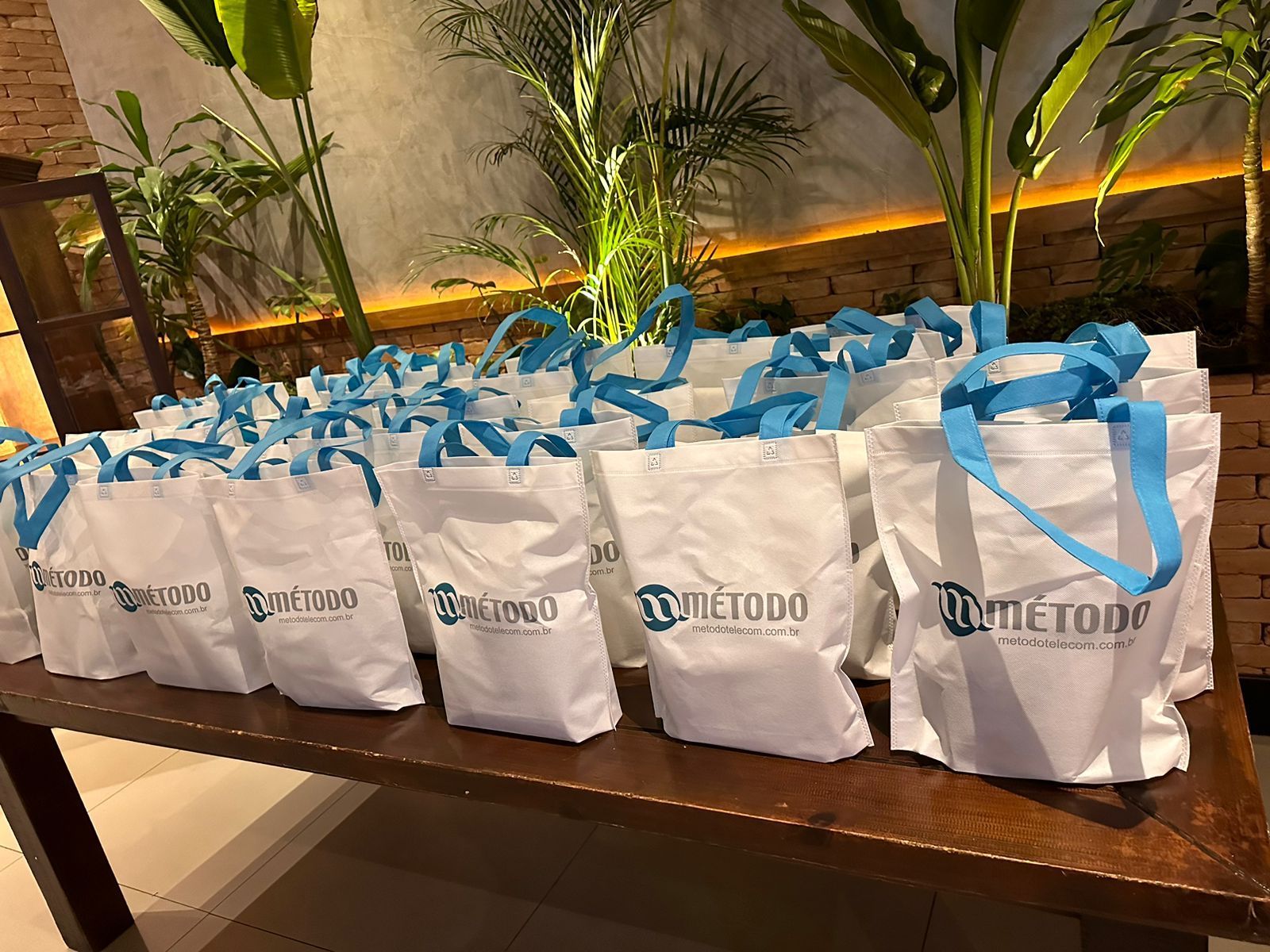 Uma fileira de sacolas brancas com alças azuis estão sobre uma mesa de madeira.