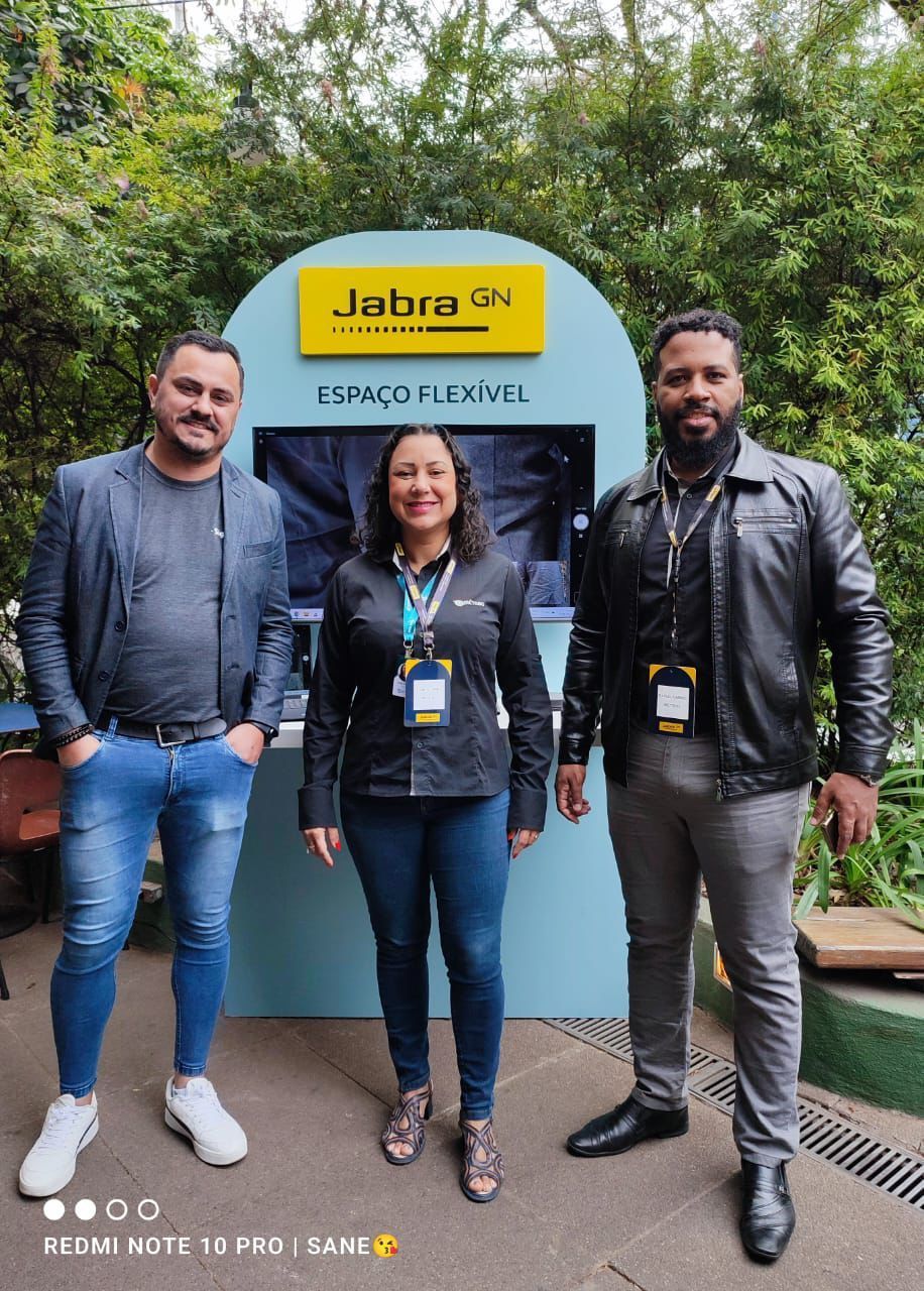 Três pessoas estão de pé, uma ao lado da outra, em frente a uma placa da Jabra.