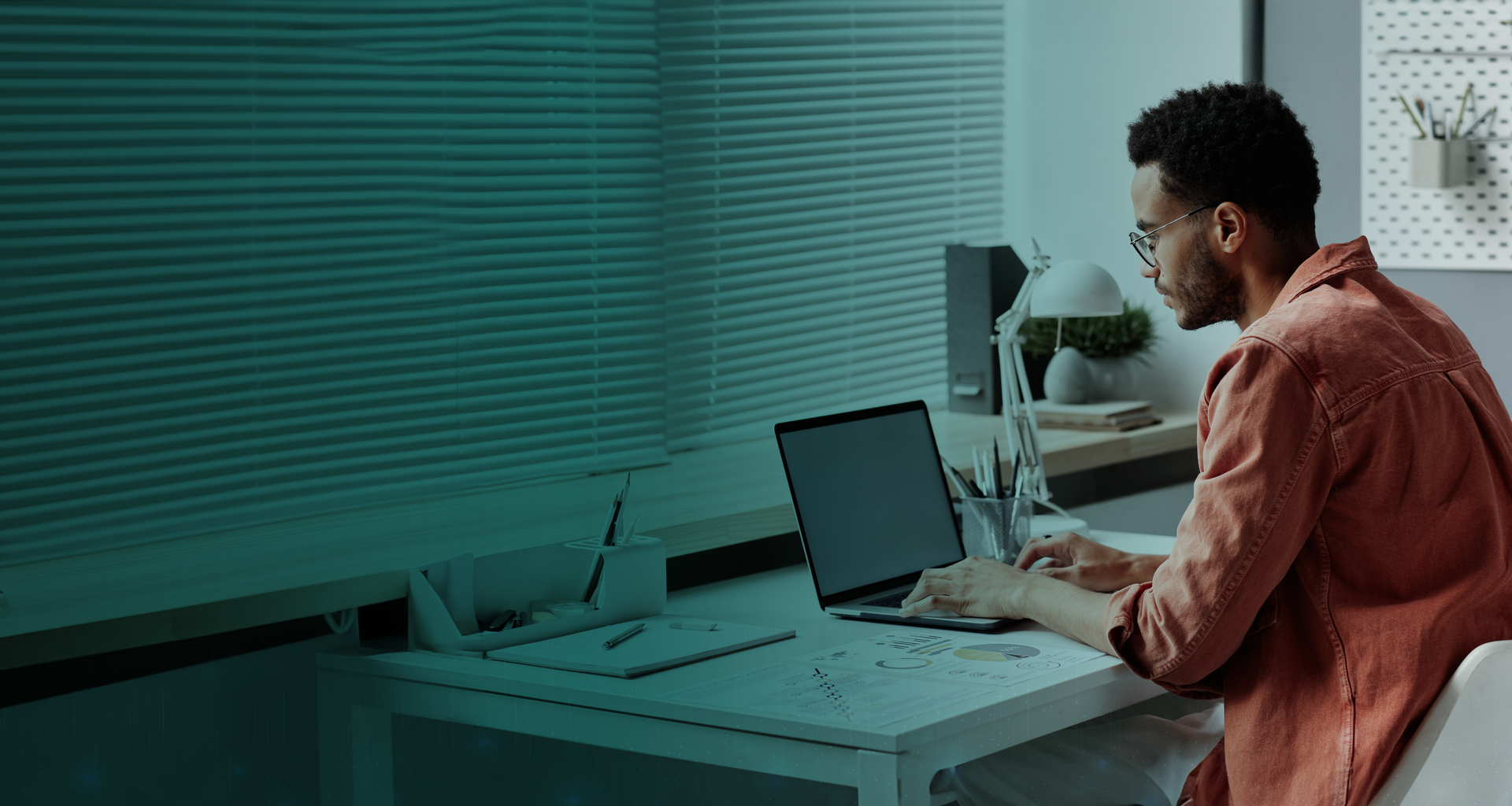 Um homem está sentado em uma mesa usando um laptop.