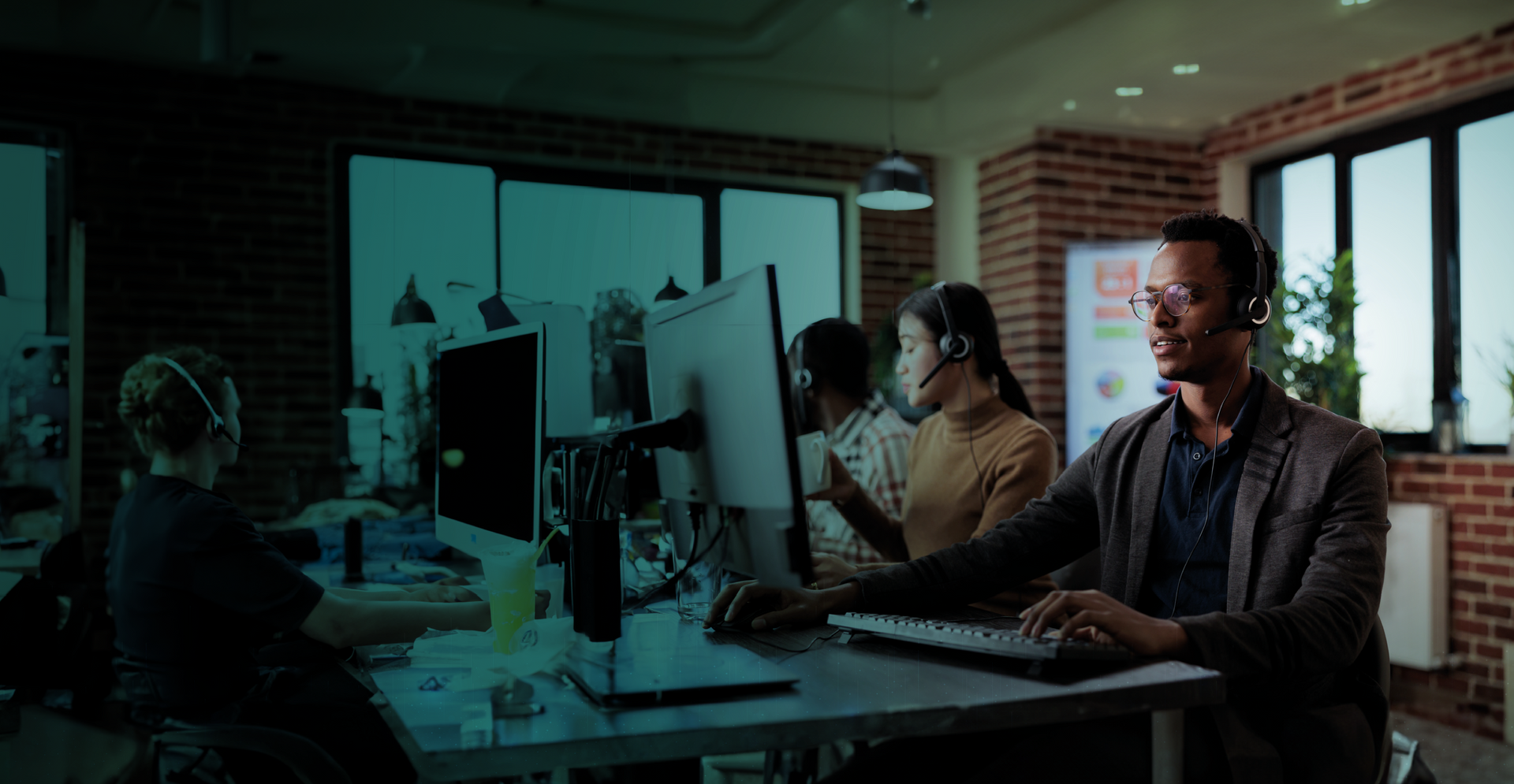 Um homem usando um fone de ouvido está sentado em uma mesa em frente a um computador.