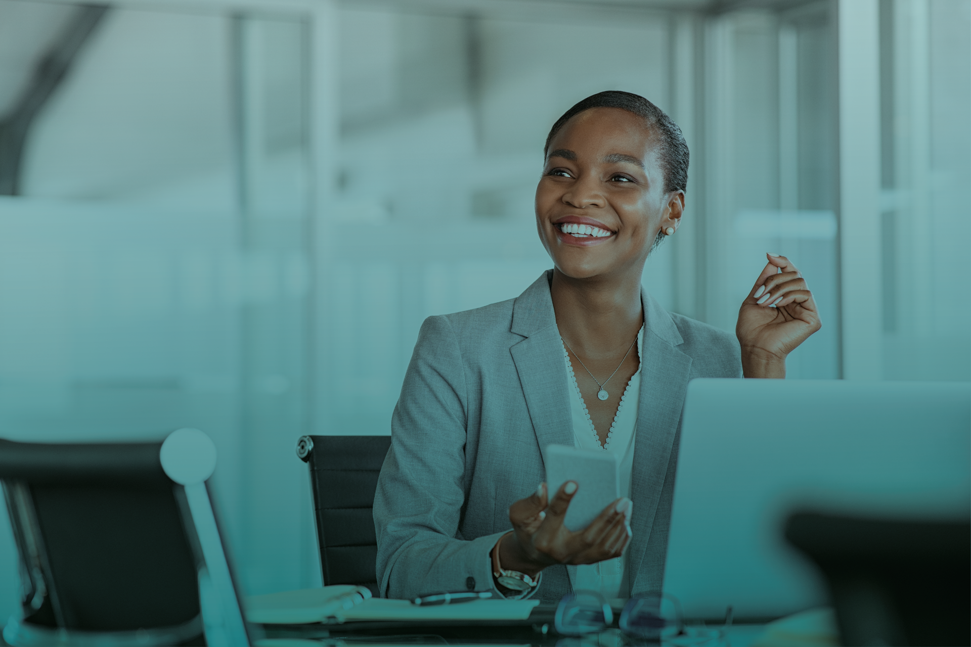 Uma mulher está sentada em uma mesa com um laptop e um celular.