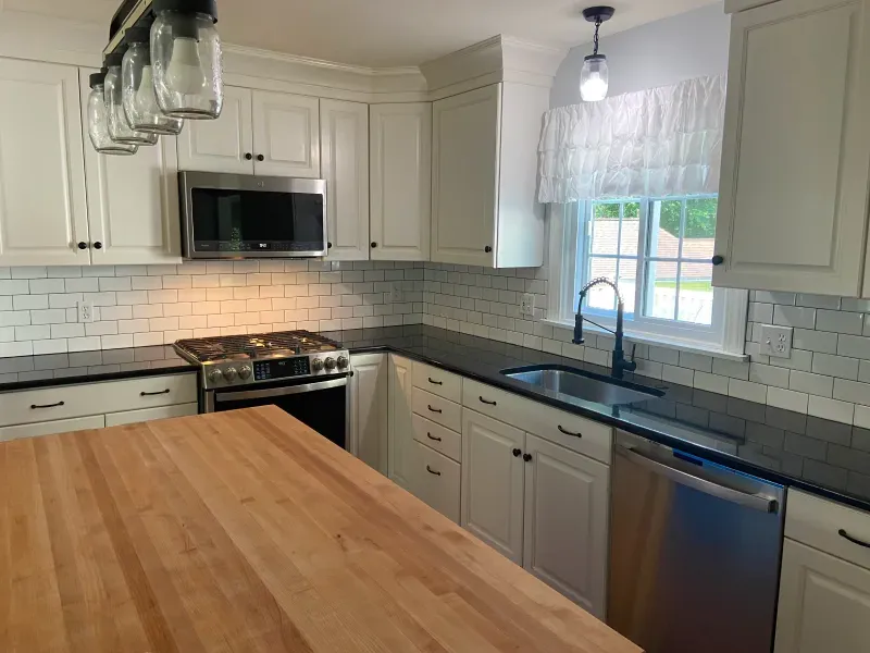 A kitchen with white cabinets , black counter tops , stainless steel appliances and a wooden island.