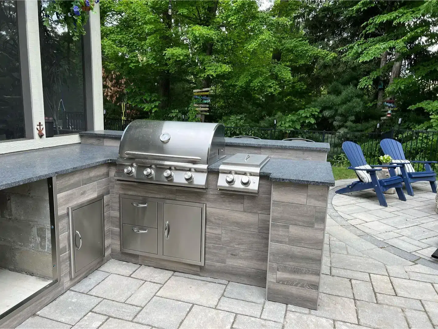 An outdoor kitchen with a grill and chairs on a patio.