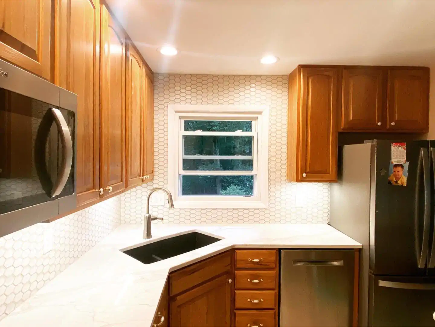 A kitchen with wooden cabinets , stainless steel appliances , a sink , and a window.