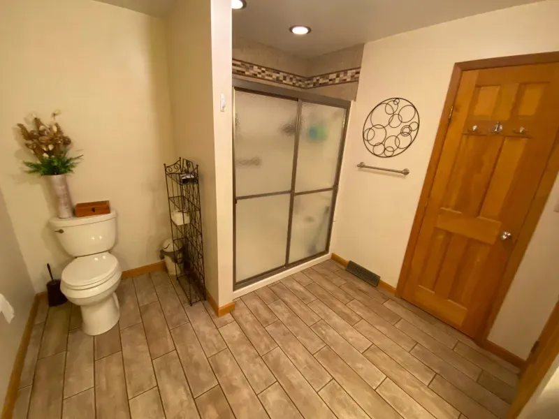 A bathroom with a toilet , shower and door.