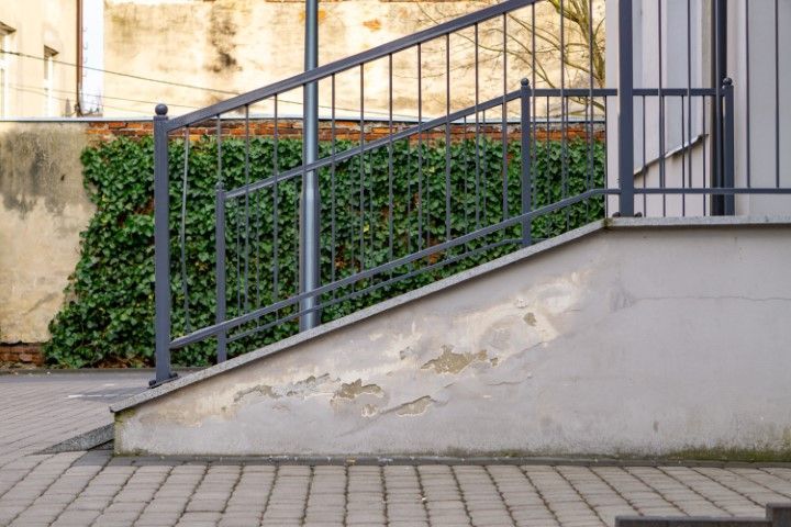 Concrete ramp, metal rail, and ivy on weathered wall