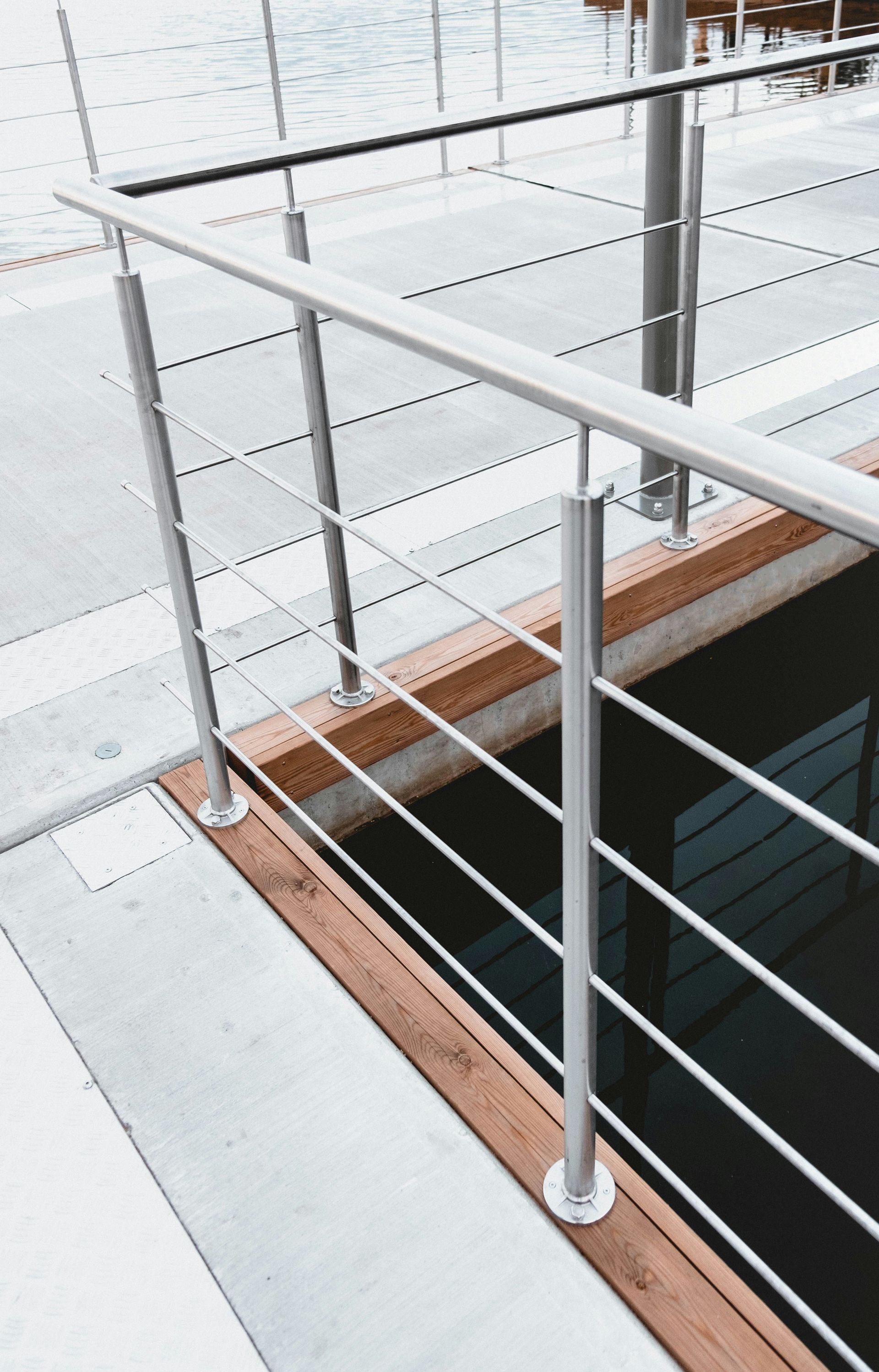 White metal railing on a balcony with a dark stair opening and wood trim along the edge.