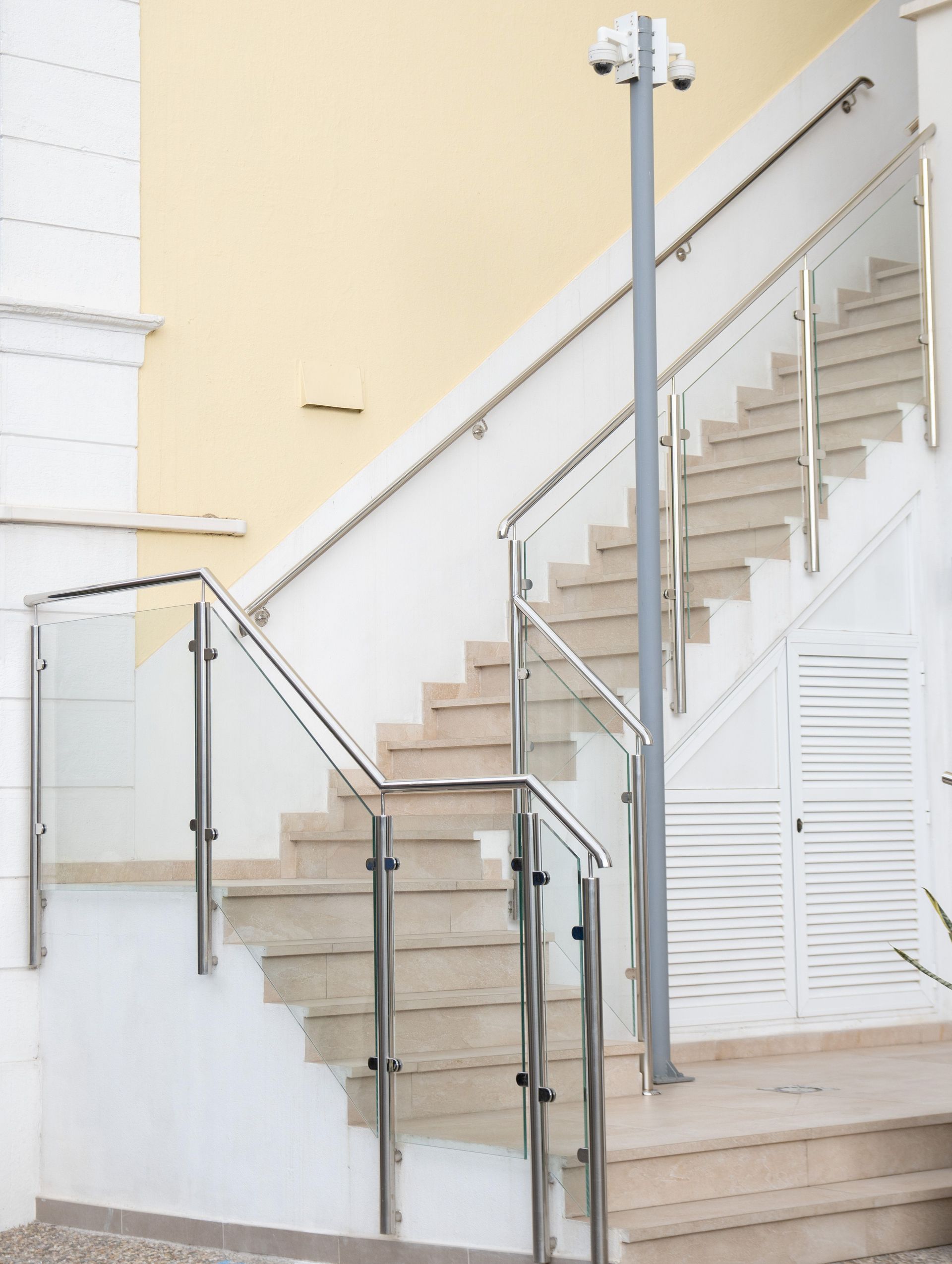 Indoor staircase with beige steps, glass railing, and white walls, viewed from below