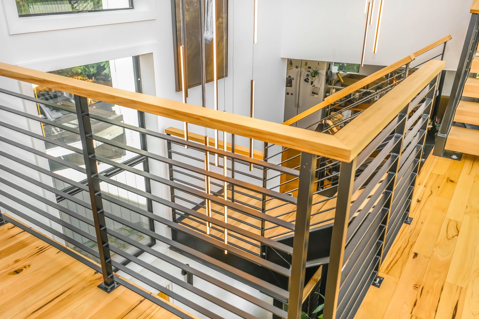 Modern staircase with black metal railing, wood handrails, and light hardwood floors in a bright home interior