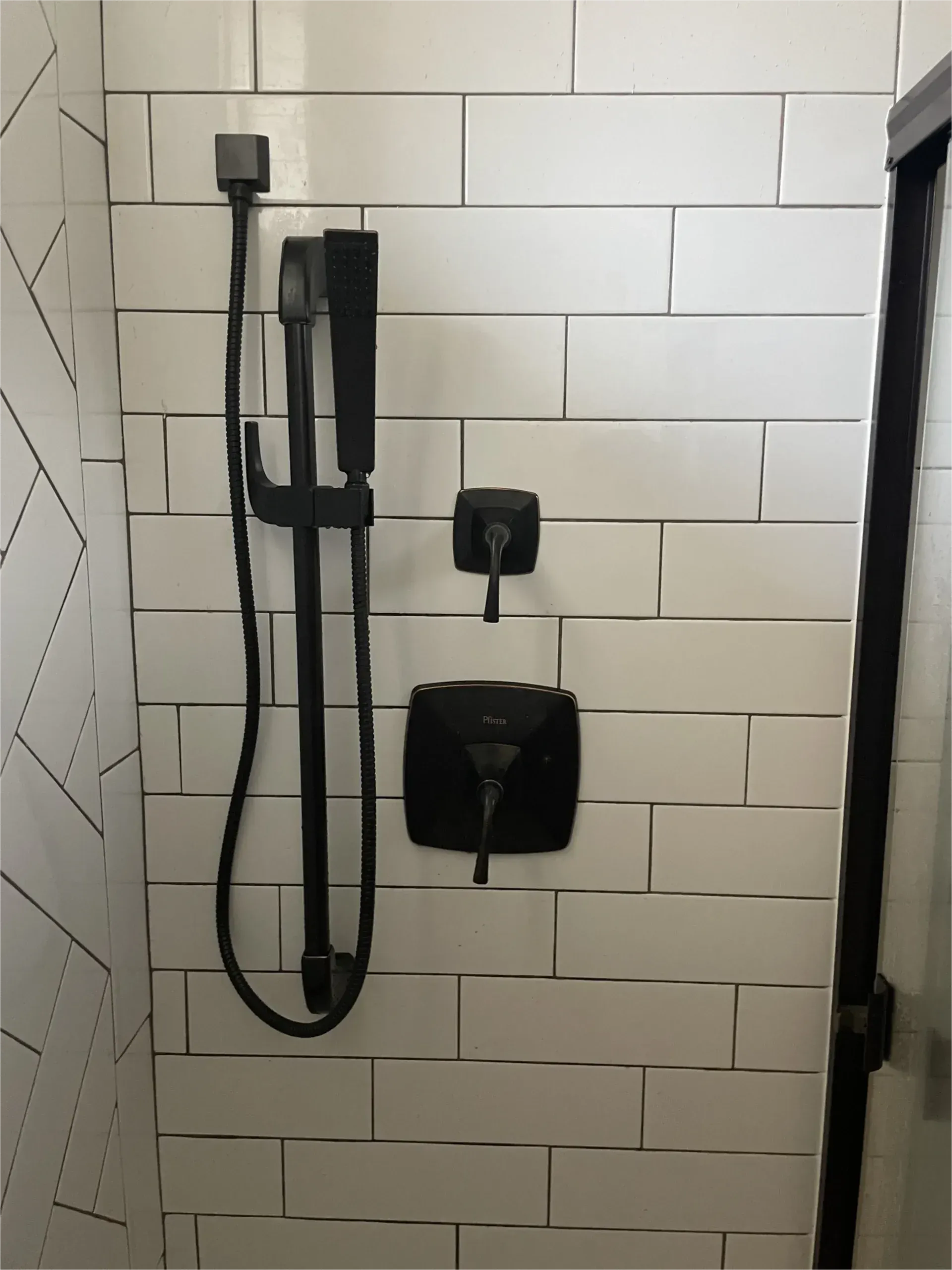 A shower with white tiles and a black shower head.