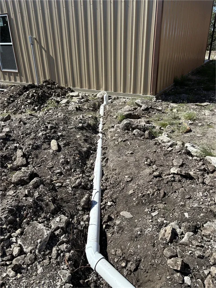 A white pipe is laying in the dirt in front of a building.